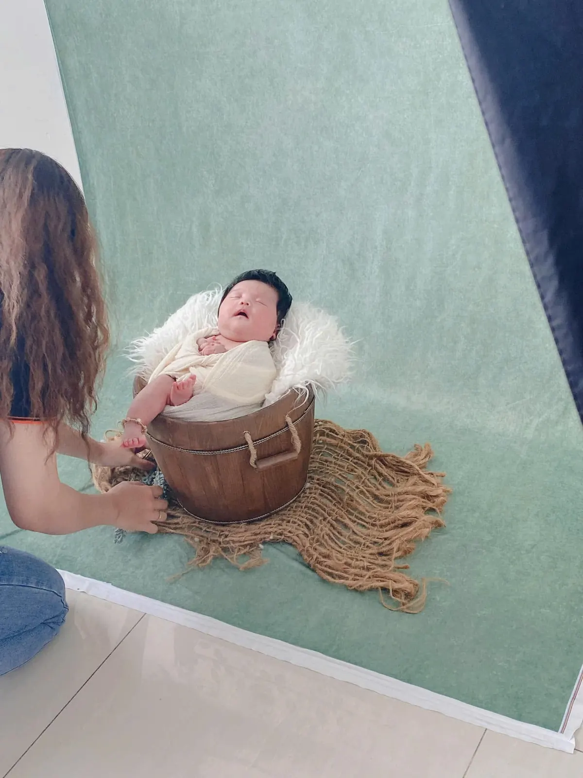 Hậu trường ekip đang hỗ trợ tạo dáng cho bé newborn chụp ảnh trong chậu gỗ.