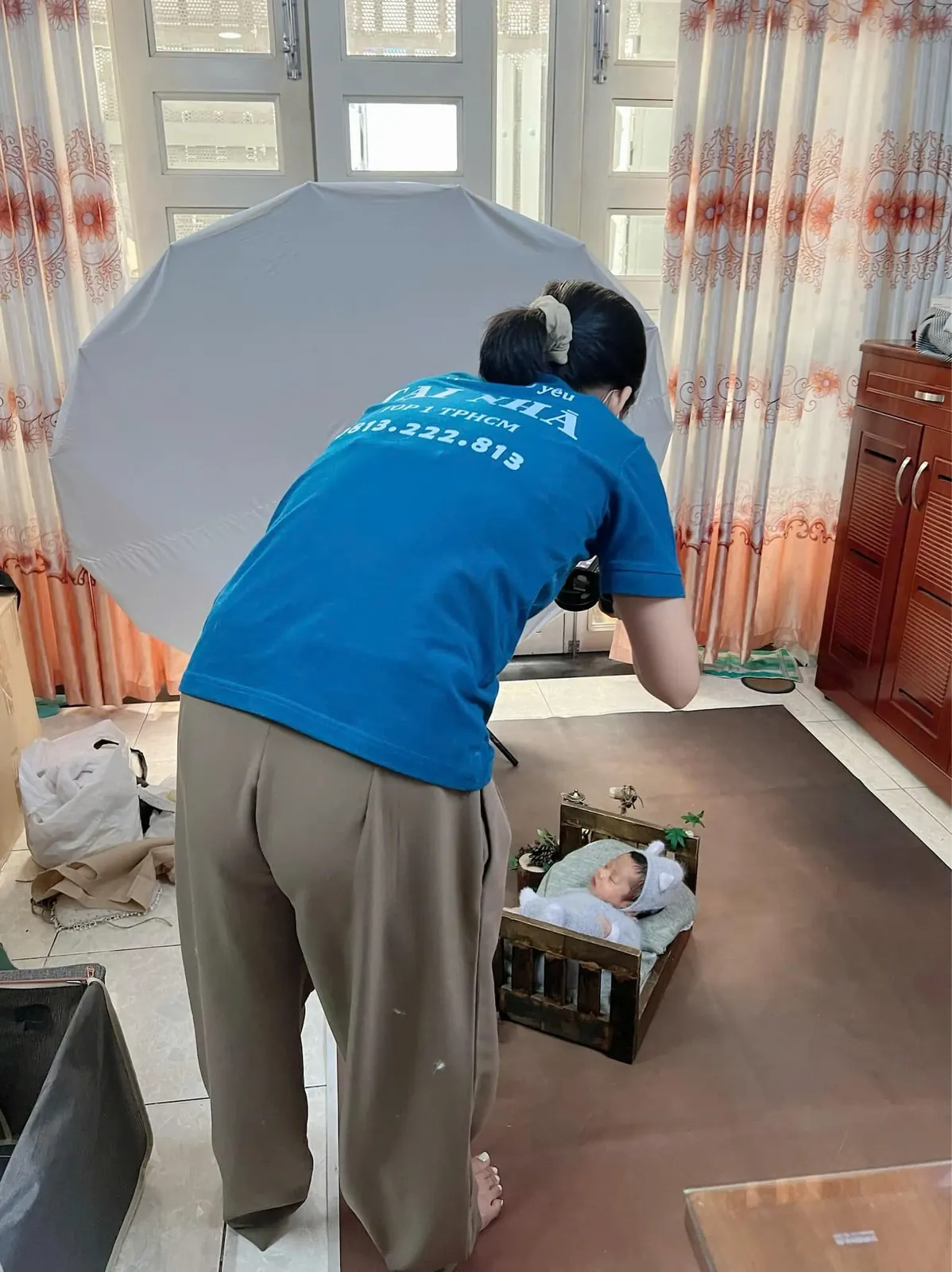 Nhiếp ảnh gia đang chụp ảnh bé sơ sinh nằm ngủ trên chiếc giường gỗ nhỏ